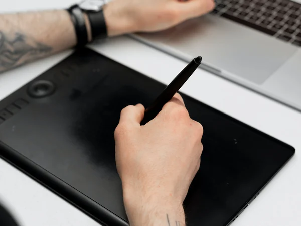 Persona usando una tableta gráfica junto a una laptop
